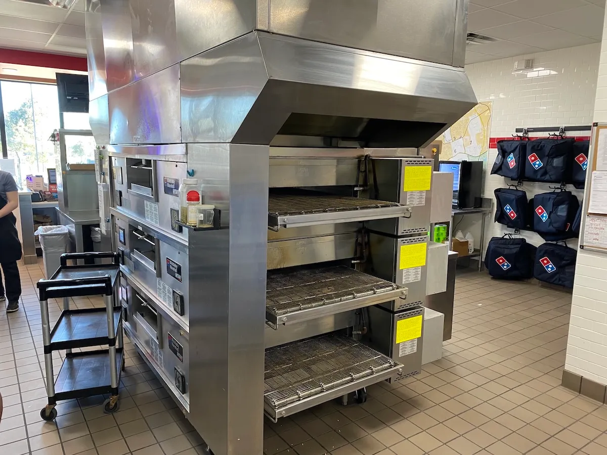 Stainless steel kitchen exhaust hood installed over triple-stack conveyor pizza ovens