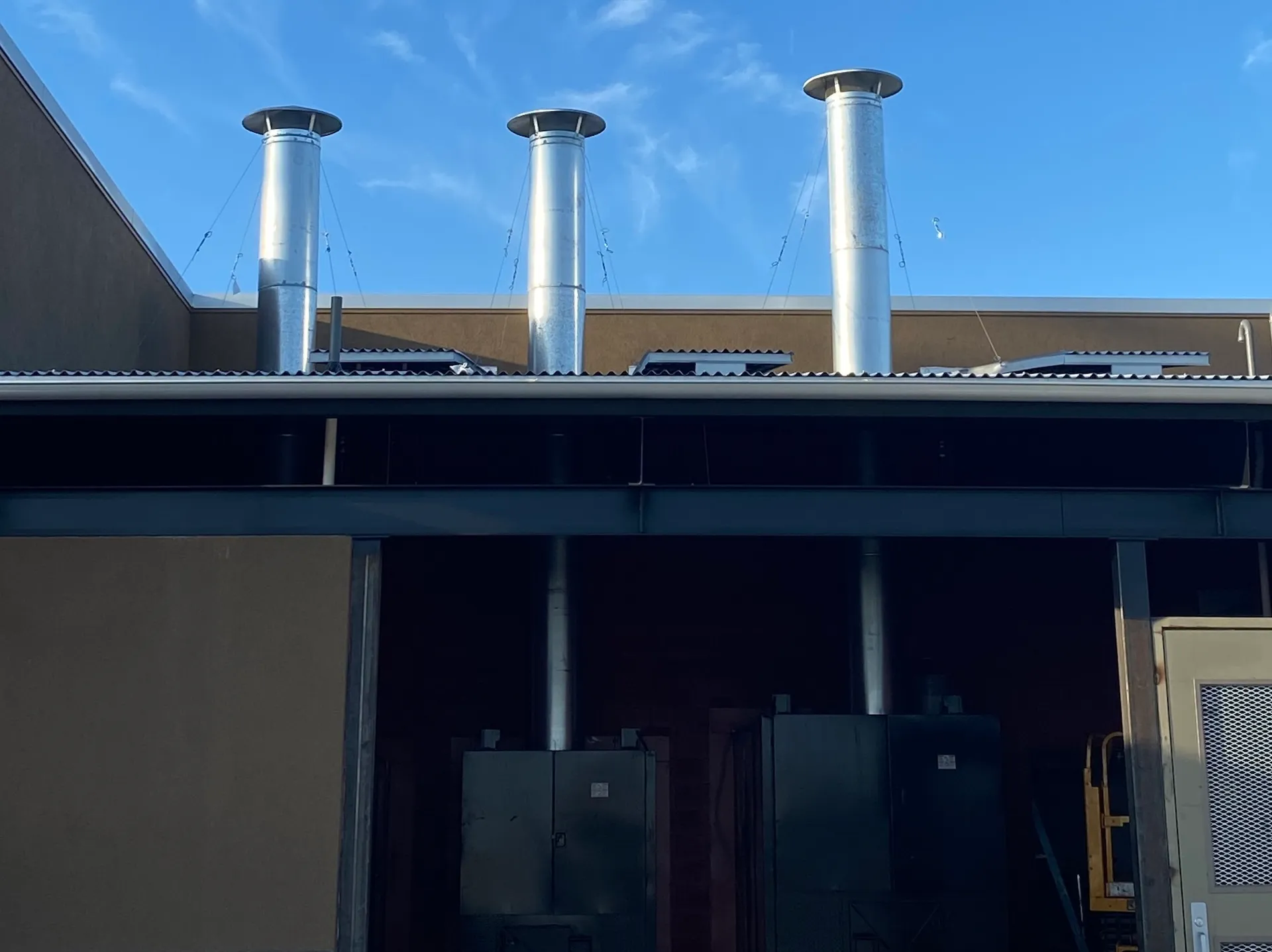Three stainless steel exhaust stacks installed along a restaurant roofline