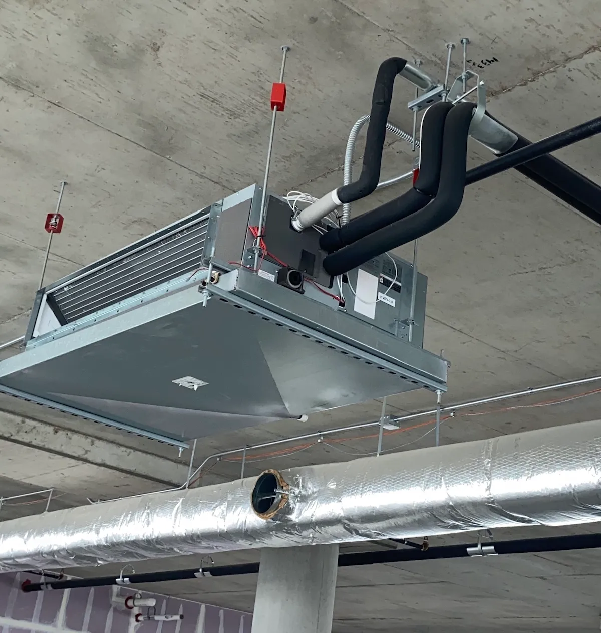 Suspended fan coil unit with insulated refrigerant piping mounted to a concrete deck